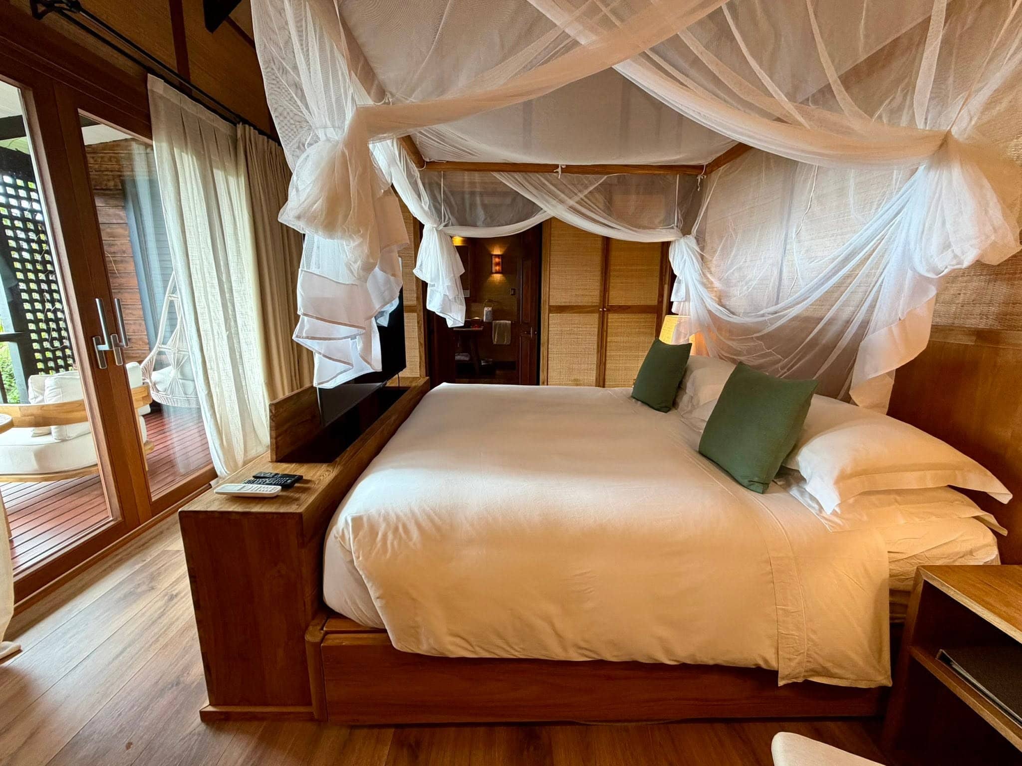 Bedroom inside a Hillside Garden Pool Villa at Hermitage Bay Antigua featuring a king bed, mosquito net canopy, wood finishes, and access to a private outdoor deck.