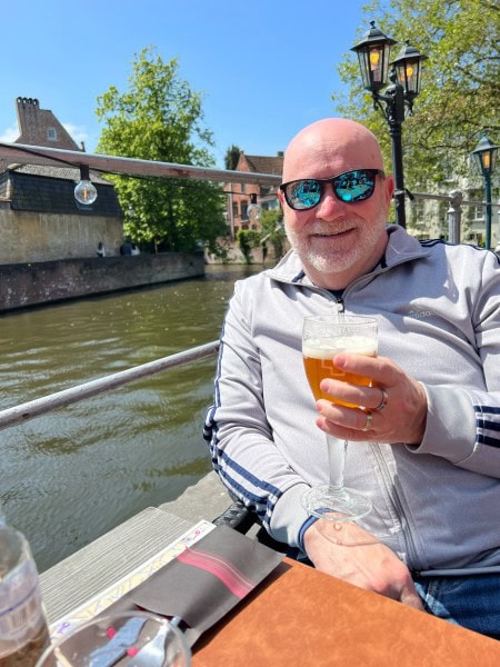 Randy enjoying a Belgian beer along a canal-side café terrace in Bruges, Belgium during a European anniversary trip