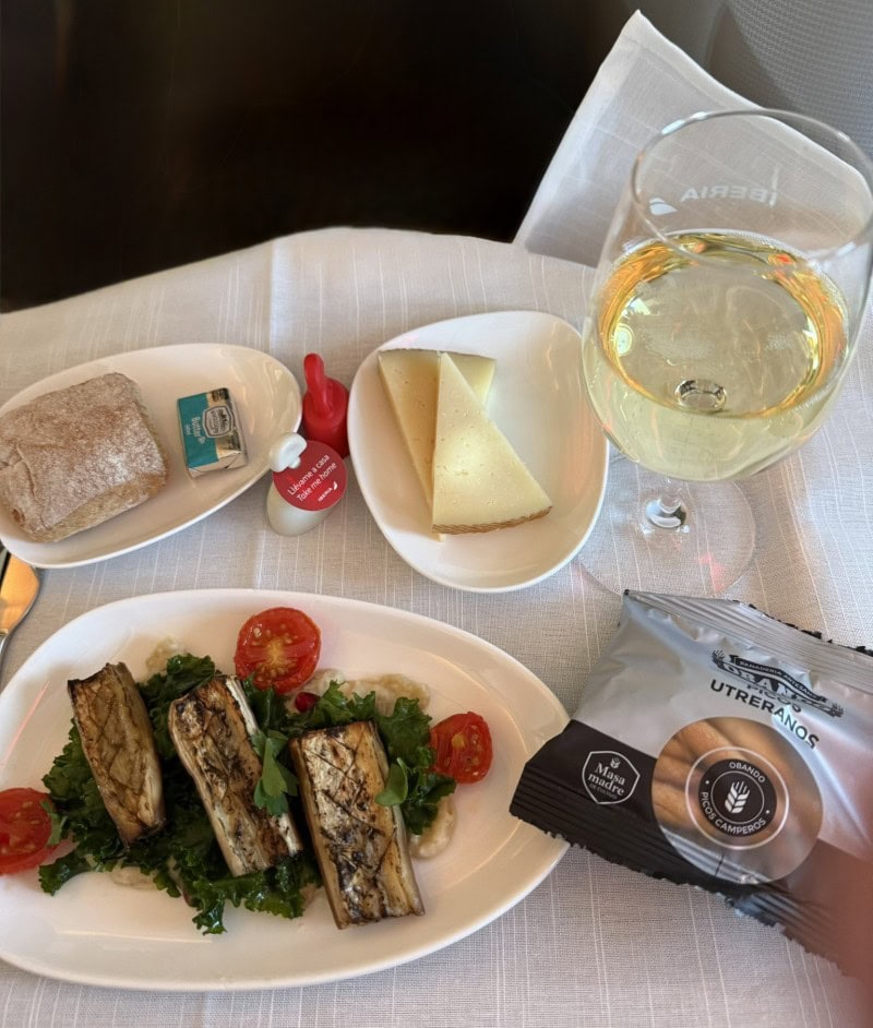 Business class meal service on an international flight, featuring a plated appetizer, wine, and premium onboard dining experience.