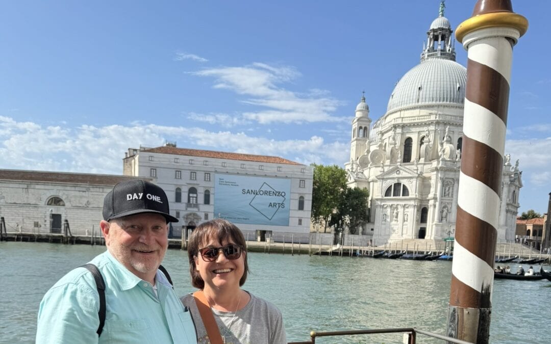 Couple standing along the Grand Canal in Venice with the Basilica di Santa Maria della Salute in the background.