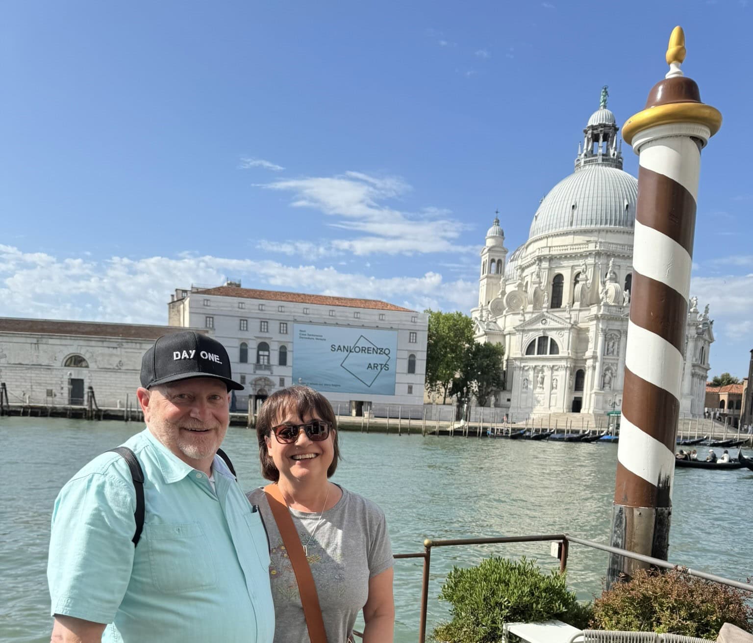 Couple standing along the Grand Canal in Venice with the Basilica di Santa Maria della Salute in the background.