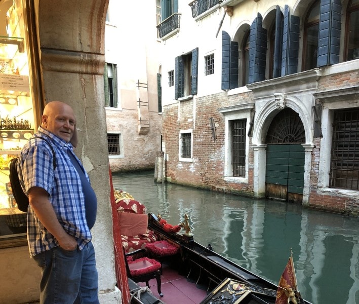 Traveler standing beside a gondola on a quiet canal in Venice, Italy