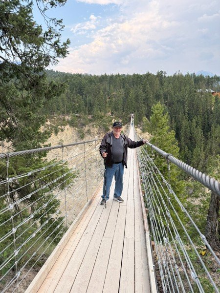 Visitor crossing the Golden Skybridge suspension bridge above a forested canyon in Golden, British Columbia