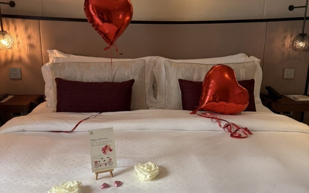 St Regis Venice bed decorated with red heart balloons, white roses, and an anniversary card