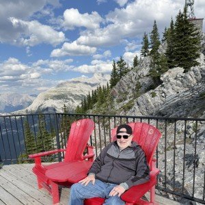 Randy relaxing in a red Adirondack chair on Sulphur Mountain during Day 4 in Banff