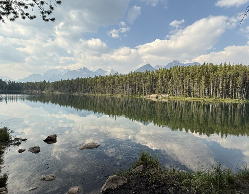 Calm Herbert Lake reflecting evergreen forest, mountains and clouds