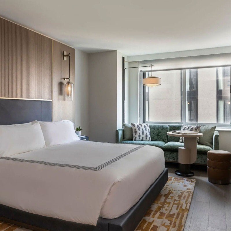 King room at Thompson Central Park New York with a king bed, green sofa, round table, and large window.